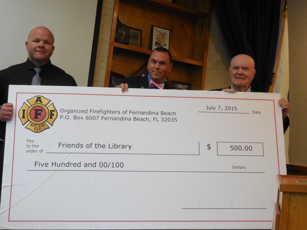 Firefighters Chett Lyncker (l) and James Tucker (r) present $500 check to Friends of Library on behalf of Organized Firefighters.